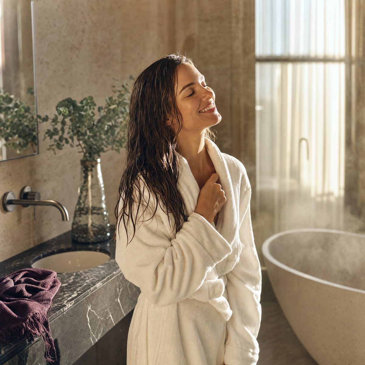 Woman in a white robe with wet hair, smiling after a shower